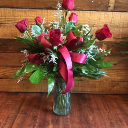 Red roses arranged in a clear glass vase with a pink ribbon
