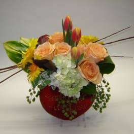 Peach roses and yellow flowers in a red vase