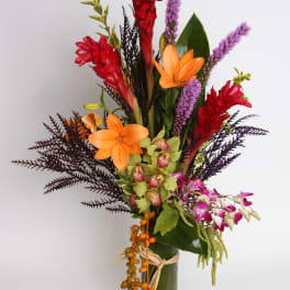 Tropical bouquet with orange lilies, red ginger, and purple orchids in a glass vase