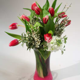 Pink tulips and white flowers in a tall glass vase