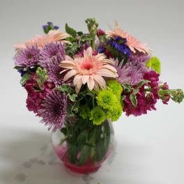 Mixed bouquet of pink, purple, and green flowers in a glass vase