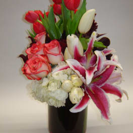 Bouquet of red tulips, pink roses, white lilies, and hydrangea in a dark vase