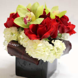 Red roses and pale green orchids in a black square vase with white hydrangeas