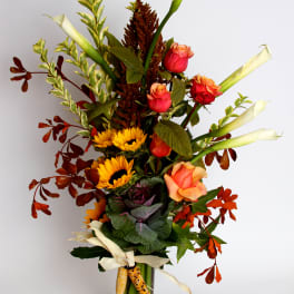 Tall mixed bouquet with roses, sunflowers, and white calla lilies in a glass vase