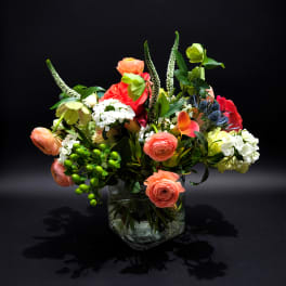 Mixed bouquet of coral, white, and green flowers in a clear glass vase