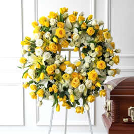 Yellow and white floral wreath on an easel beside a casket