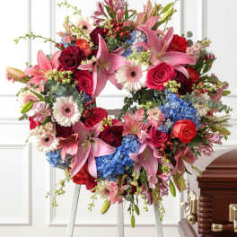 Heart-shaped floral wreath with pink lilies, roses, and blue hydrangeas on an easel