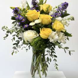 Mixed bouquet of yellow and white roses with purple flowers in a clear glass vase