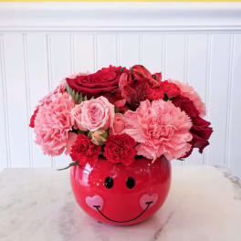 Pink and red flower arrangement in a smiley-face vase