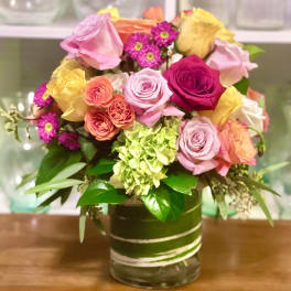 Mixed bouquet of pink, yellow, and orange roses in a glass vase