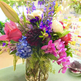 Colorful mixed bouquet in a clear glass vase with lilies, orchids, and hydrangeas