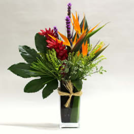 Tropical flower arrangement in a tall glass vase with orange and red blooms