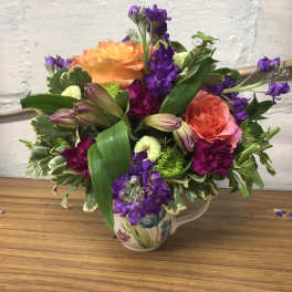 Colorful bouquet of orange and purple flowers in a floral ceramic pitcher