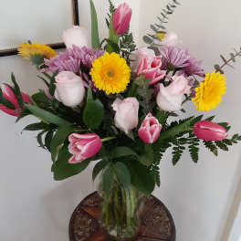 Pink tulips and roses with yellow daisies in a glass vase