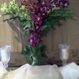 Tall orchid arrangement in purple and green with a glass vase