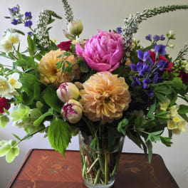 Mixed bouquet of pink, peach, white, and purple flowers in a clear glass vase