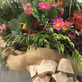 Mixed bouquet with pink and red flowers in burlap wrapping and a large beige bow