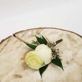 White rose boutonniere with small white blossoms on a wood slice