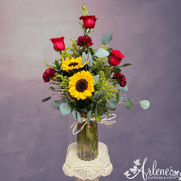 Tall bouquet of red roses and yellow sunflowers in a glass vase