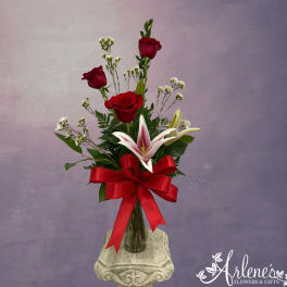 Red roses and a lily in a glass vase with a red ribbon