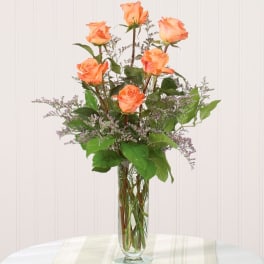Orange roses in a tall clear glass vase with purple filler flowers