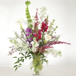 Tall mixed bouquet in a clear glass vase with white calla lilies and red, pink, and purple blooms