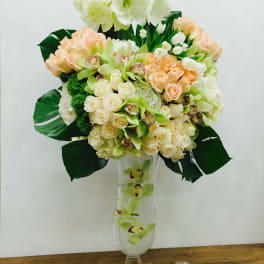 Tall bouquet of cream and peach flowers in a clear glass vase