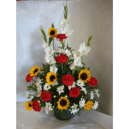 Tall arrangement of sunflowers, red carnations, white gladiolus, and daisies in a vase