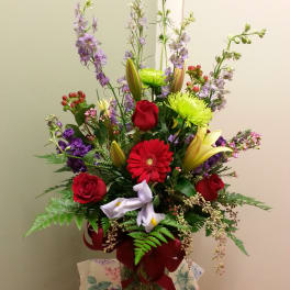 Tall mixed bouquet in a glass vase with red roses, lilies, and purple flowers