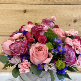 Pink and purple mixed flower arrangement in a round hat box with ribbon