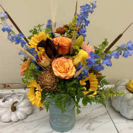 Mixed bouquet in a blue vase with sunflowers, roses, and blue delphinium