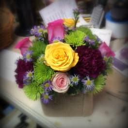 Mixed bouquet with yellow, pink, and purple flowers in a burlap-wrapped container