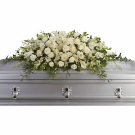 Long white casket spray with roses, calla lilies, and other blooms on a silver casket