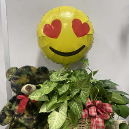 Potted green plants in a wicker basket with a teddy bear and heart-eyes balloon