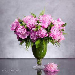 Pink peonies arranged in a tall glass vase with fern foliage