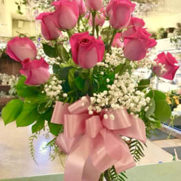 Pink roses arranged in a clear glass vase with a pink ribbon bow