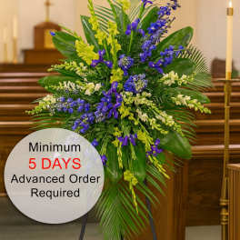 Tall standing spray of blue and yellow flowers with lush foliage on an easel in a church.