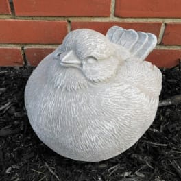 White bird-shaped garden statue resting on dark mulch in front of a brick wall