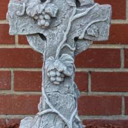 Stone cross sculpture with grape clusters against a brick wall