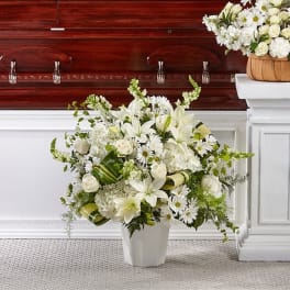 White floral arrangement in a white vase beside a casket