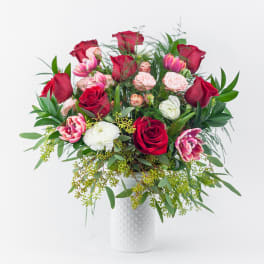Bouquet of red and pink roses with white blooms in a white vase