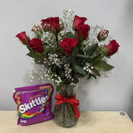 Red roses in a glass vase with a bag of Skittles candy