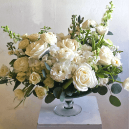 Low arrangement of white roses and other white blooms in a glass pedestal bowl