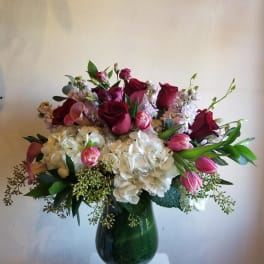 Bouquet of red roses, pink tulips, and white hydrangeas in a green glass vase