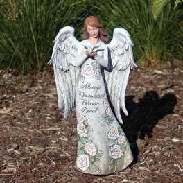 White angel statue with roses and memorial text standing outdoors