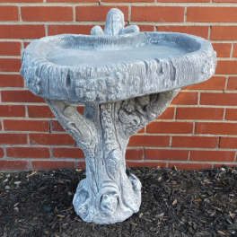 Stone birdbath with an ornate pedestal against a brick wall