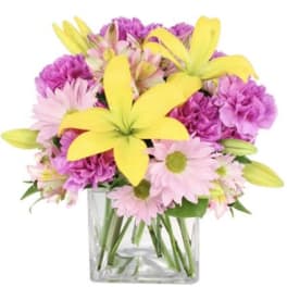 Pink and purple flowers with yellow lilies in a clear glass vase