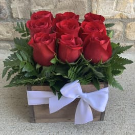 Red roses arranged in a wooden box with a white ribbon