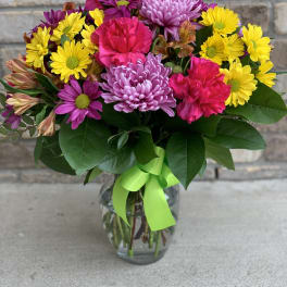 Colorful bouquet of daisies and carnations in a glass vase with a green ribbon