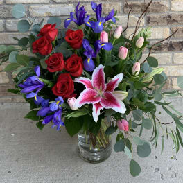 Bouquet of red roses, purple irises, pink tulips, and a pink stargazer lily in a glass vase